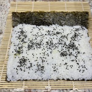 Image of sushi rice on nori with sesame seeds added