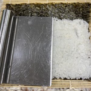 Image of sushi rice being spread with a scrapper - cutter tool
